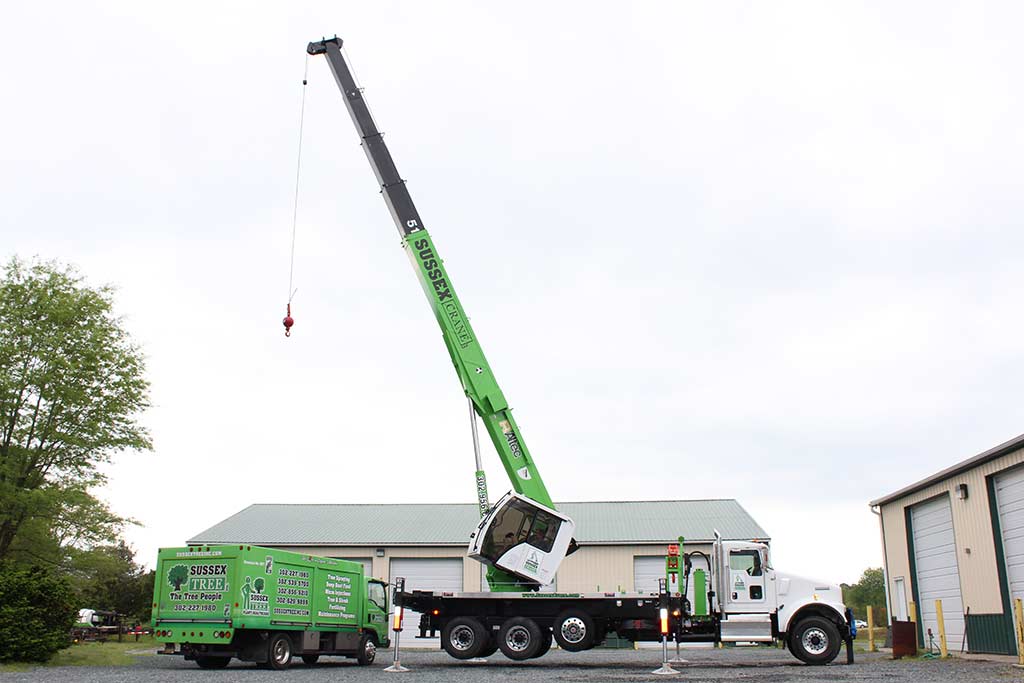 Crane in use hovering over large green truck